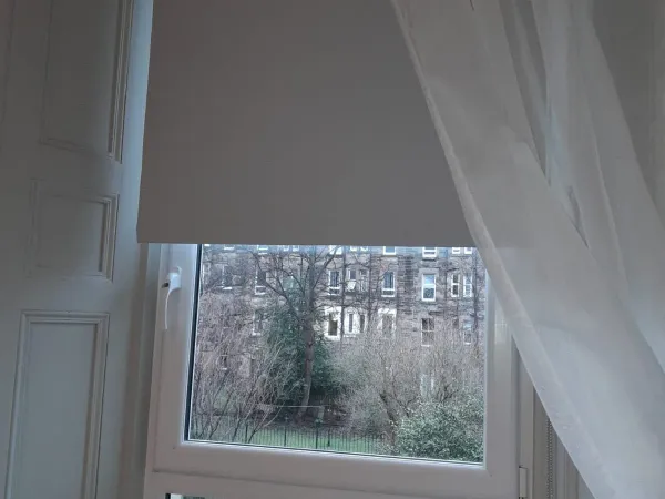 Grey roller blind paired with sheer voile curtains in an Edinburgh tenement bay window