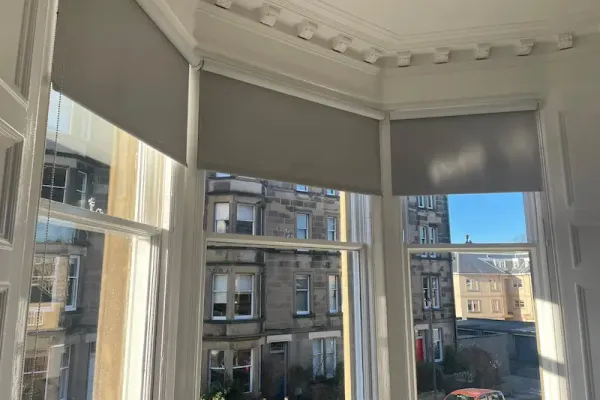 Grey roller blinds on an Edinburgh bay window overlooking traditional tenements