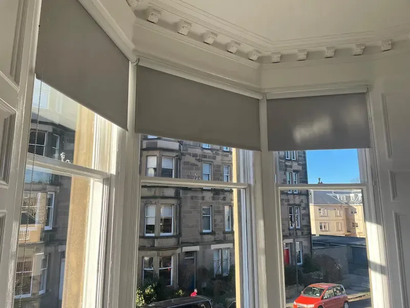 Grey roller blinds fitted on an Edinburgh bay window with traditional tenement views