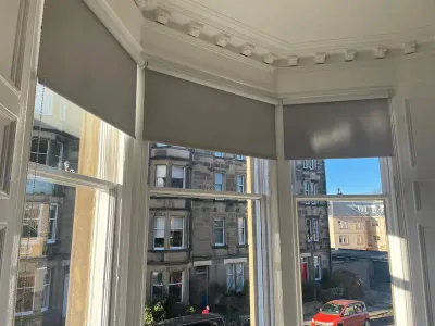 Grey roller blinds on an Edinburgh bay window with tenement views