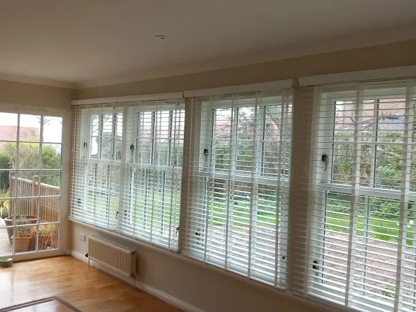 White venetian blinds in a sunroom with garden view